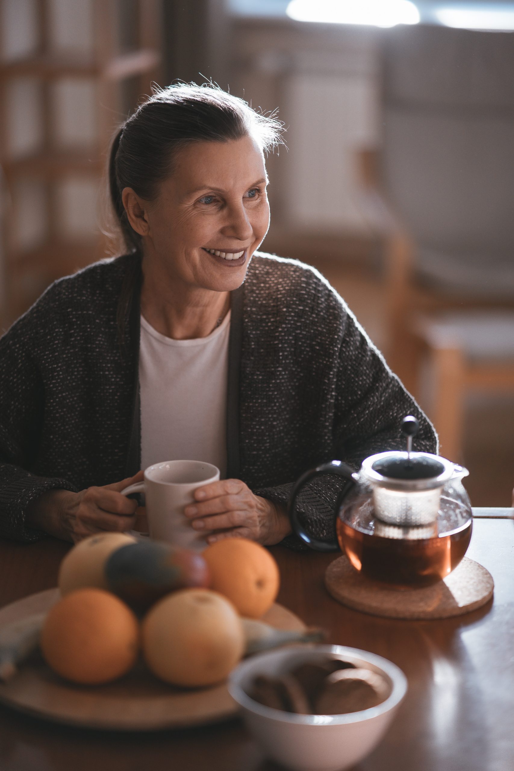 middle-aged woman sitting at a kitchen table drinking hot tea smiling